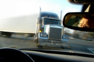 A male driver is inside a car and sees an 18-wheeler approaching head-on