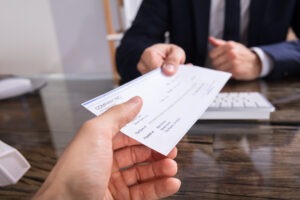 Close up,of,a,businessperson’s,hand,giving,cheque,to,colleague,at