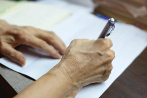 Selective,focus,at,elderly,hand,using,blue,pen,to,writing