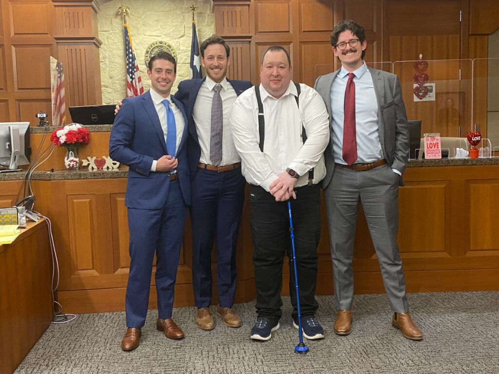 Group photo of attorneys Neil Solomon, Ben Abbas, and Max Massey, and their client Chris celebrating the successful resolution of a $15.4 million case. The attorneys and client are smiling and standing together, exuding a sense of accomplishment and professionalism.