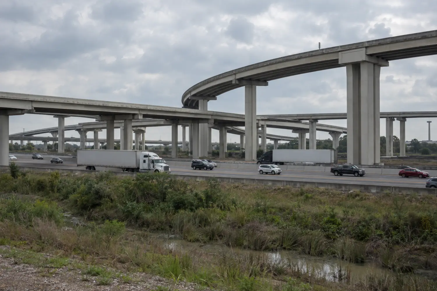 Tractor trailers and cars on a multi-level freeway interchange under an overcast sky
