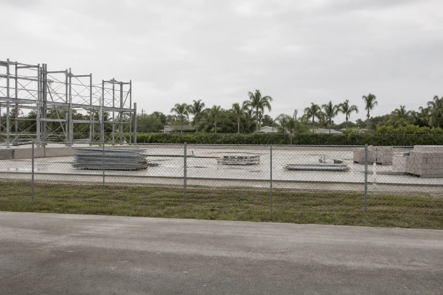 An unoccupied Florida construction site behind a chain-link fence, with scaffolding and stacked materials.