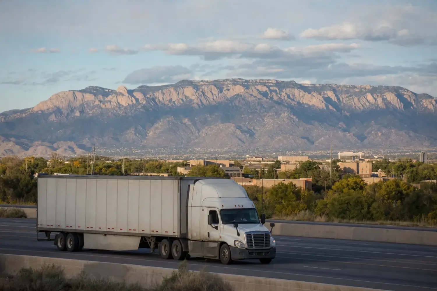 Tractor-trailer on an interstate with cottonwoods and a long mountain ridge rising behind the city