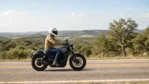 A motorcycle rider in a white helmet rides in the lane of a two-lane Texas hill country road.