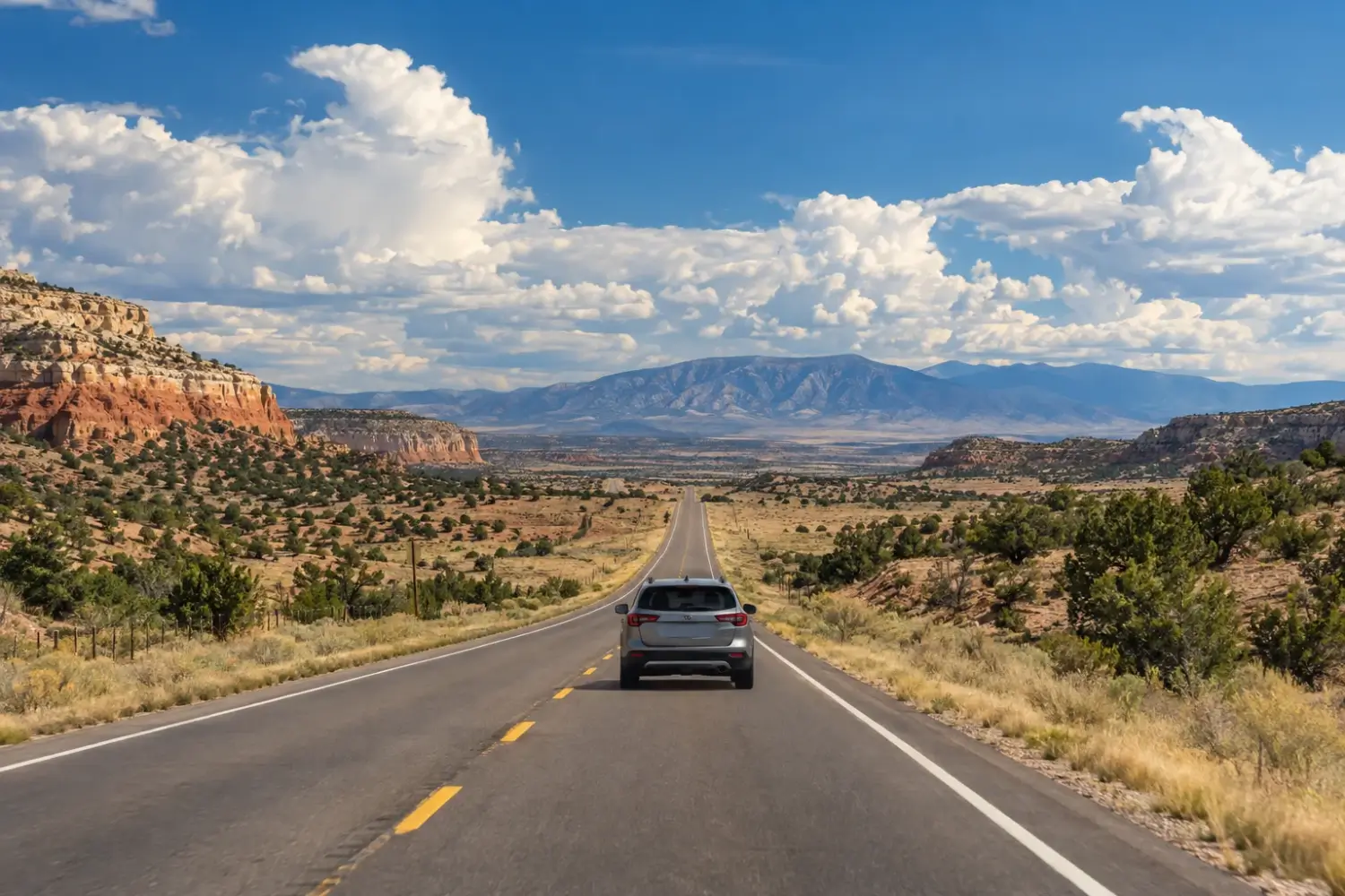 Car on an open two-lane highway through the New Mexico high desert with mesas and distant mountains