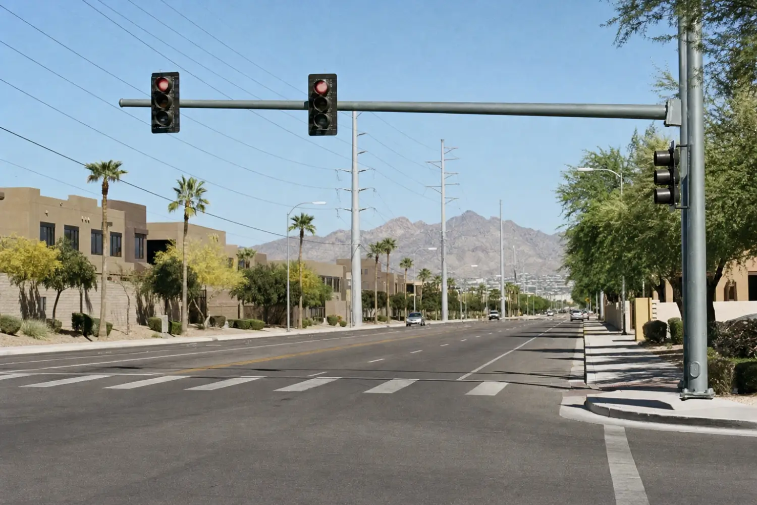 Signalized city intersection with an empty crosswalk, palm trees and dry mountains in the distance